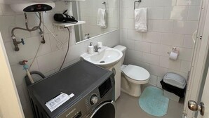 A compact bathroom with a washing machine, sink, toilet, and a mirror. - Departamentos Egaña (Puerto Montt)
