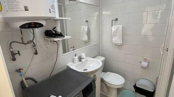 Un baño pequeño con lavadora, lavamanos, inodoro y espejo.