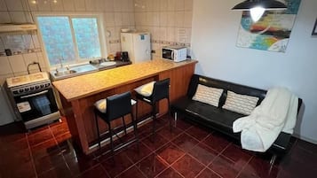 Una cocina compacta con una isla central, un área de comedor con un sofá y una silla negra.