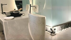 Un baño moderno con un lavamanos curvo, una cabina de ducha con mampara de vidrio y un espejo grande.