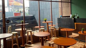 Un interior de cafetería con mesas y sillas de madera, ventanas amplias y una pared de acento verde.