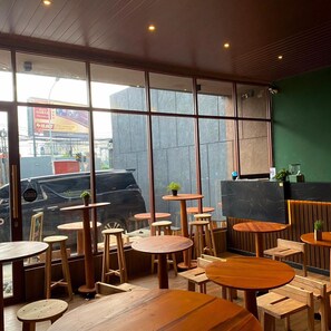 Interior de café com mesas e cadeiras de madeira, janelas amplas e uma parede verde destacada.