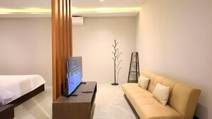Una habitación de hotel moderna con cama, sofá, televisor sobre un pedestal y una lámpara de pie.