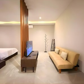 Quarto de hotel moderno com cama, sofá, TV em suporte e luminária de chão.