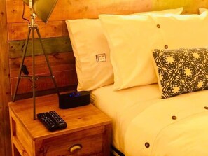 A wooden nightstand with a lamp, a remote control, and a power strip. - DT Loft (Natales)