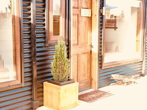 A wooden door with a number plate, a small potted plant, and a window with horizontal blinds. - DT Loft (Natales)