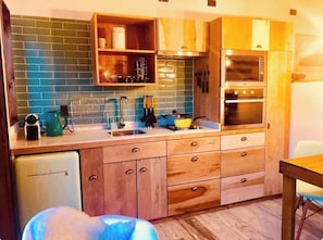 A compact kitchen with wooden cabinets, a built-in oven, and a small refrigerator. - DT Loft (Natales)