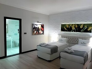 Een moderne hotelkamer met een groot bed, twee kleinere bedden, een badkamer en een groot raam.