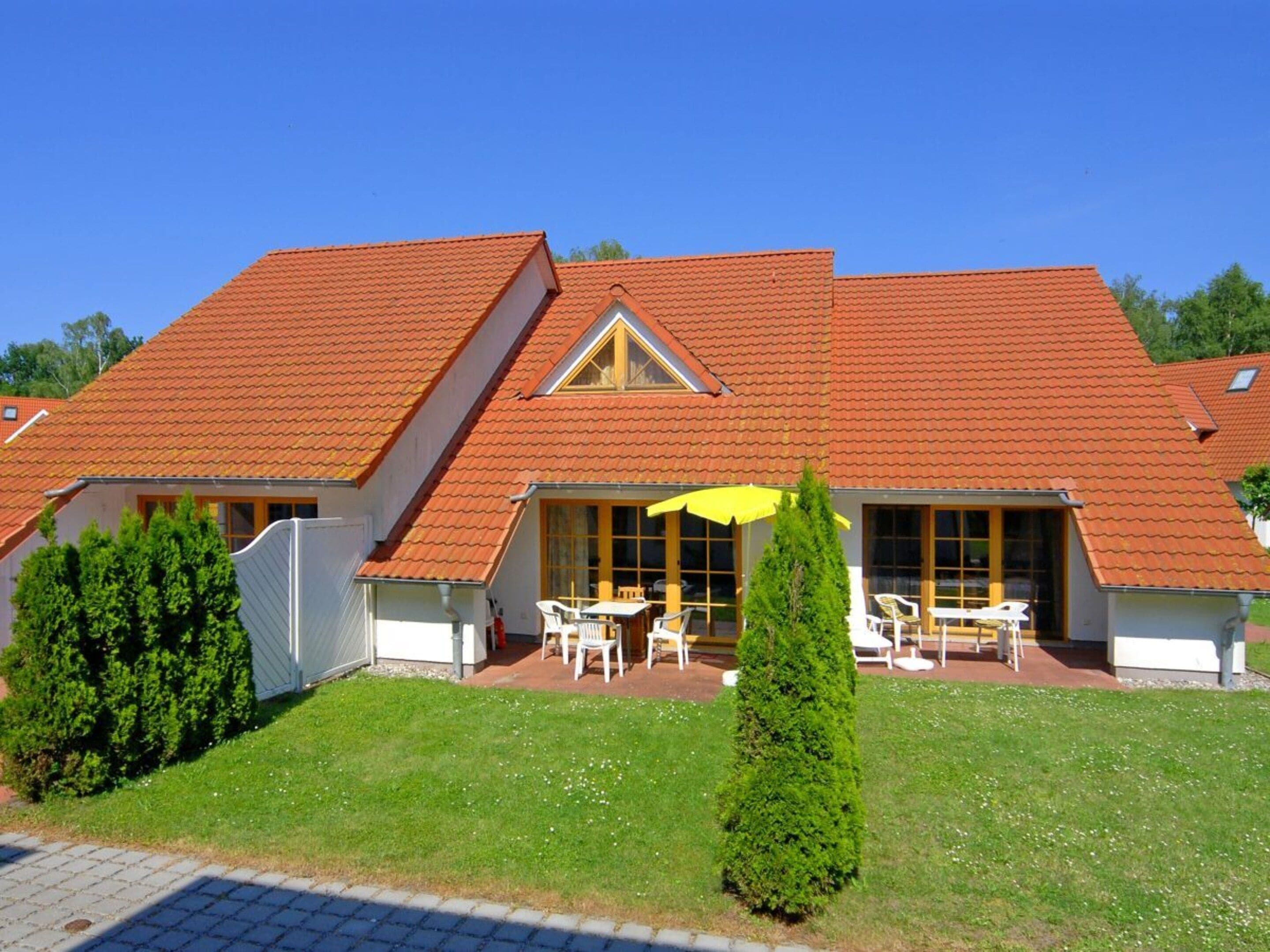 A two-story house with a red-tiled roof, a covered patio with outdoor furniture, and a well-maintained lawn.