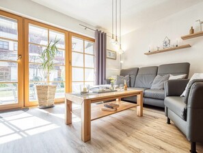 A modern living room with a sofa, a coffee table, and a large window with curtains. - 6a/t5 in the "freesenbruch" Holiday Park (Zingst)