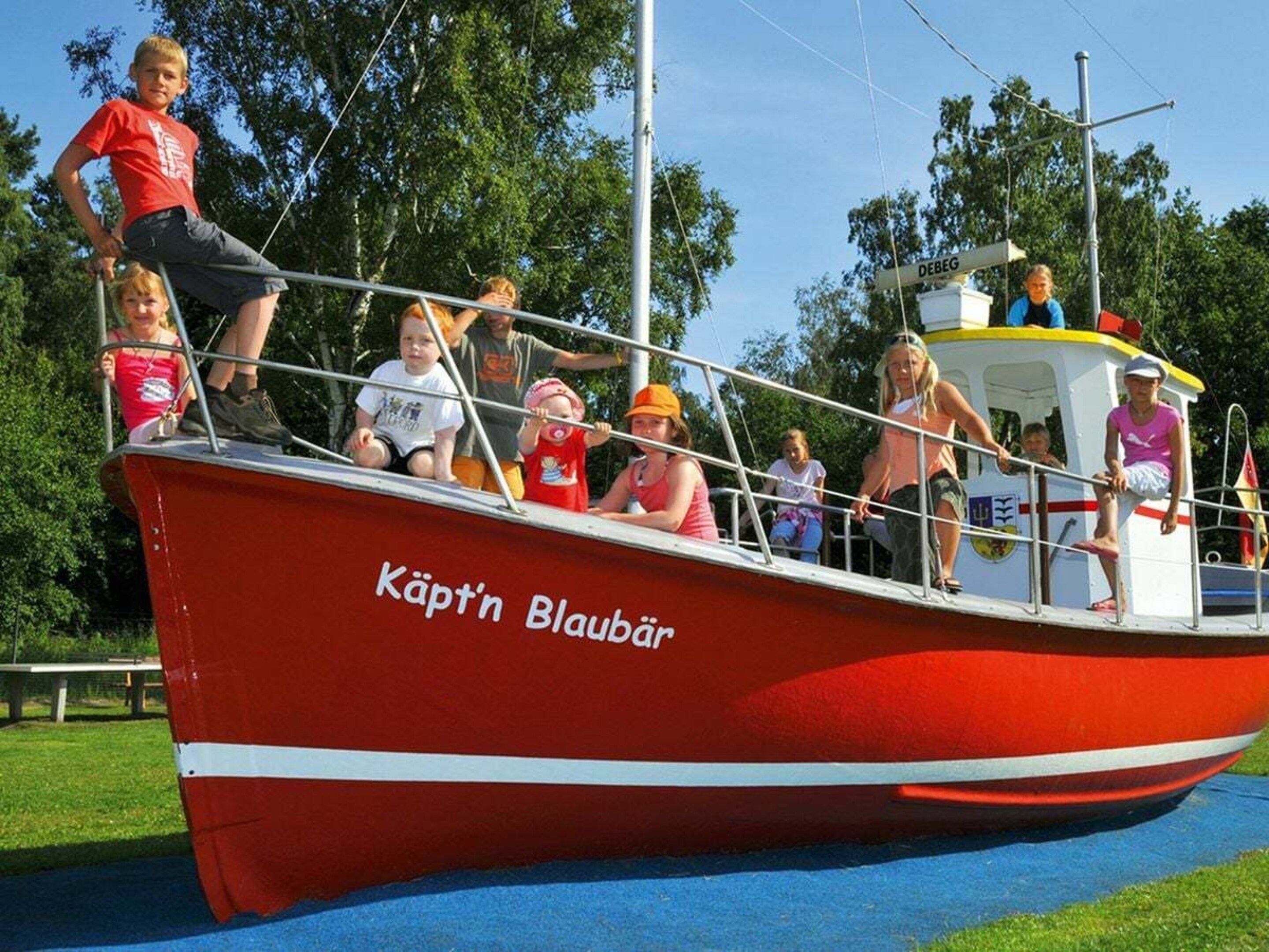 Een rode boot met de naam 'Käpt'n Blaubär' aan de zijkant, afgemeerd aan een steiger met mensen aan boord.