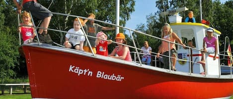 Ein rotes Boot mit dem Schriftzug 'Käpt'n Blaubär' an der Seite, liegt an einem Steg, und es befinden sich Personen an Bord.
