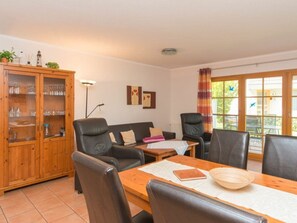 A living room with a wooden cabinet, leather sofas, a dining table with a placemat, and a window with curtains. - 1.3/t2 Holiday Home Park \"freesenbruch\" (Zingst)