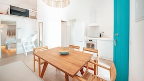 A modern kitchen with white cabinets, a teal door, and a wooden dining table with chairs. - Anemela Mykonos Villas & Suites (Mykonos)