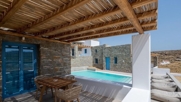 A poolside area with a wooden pergola, stone walls, and a view of the landscape. - Anemela Mykonos Villas & Suites (Mykonos)