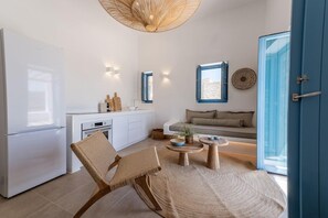 Eine moderne Küche mit weißen Schränken, einem weißen Kühlschrank und einem Essbereich mit einem gewobenen Stuhl und einem runden Holztisch.