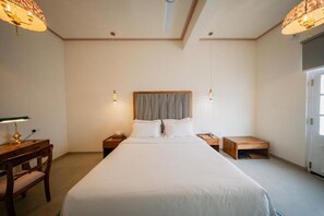 Quarto de hotel com uma cama grande, mesas de cabeceira, escrivaninha e uma cadeira.