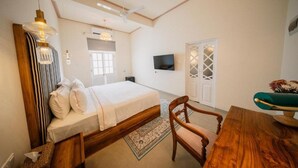 Ein Schlafzimmer mit einem Bett, einem Holzstuhl, einem Tisch, einem Fernseher und einem Deckenventilator.