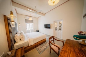 A bedroom with a bed, a wooden chair, a table, a TV, and a ceiling fan. - Padmaraga Galle Fort (Galle)