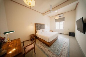 A bedroom with a bed, bedside table, lamp, chair, and a television on the wall. - Padmaraga Galle Fort (Galle)