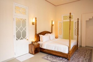 A four-poster bed with a wooden frame and white bedding, a nightstand with a lamp, and a patterned rug on the floor. - Padmaraga Galle Fort (Galle)