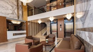 Un hall d’entrée avec un comptoir de réception, un espace salon, un escalier, des ascenseurs et un lustre.