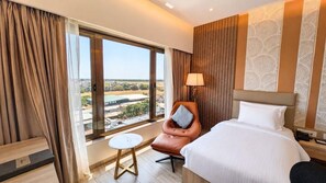 A hotel room with a bed, a chair, a small table, and a view of the cityscape through large windows. - Pride Elite Chhatrapati Sambhajinagar (Chhatrapati Sambhajinagar)