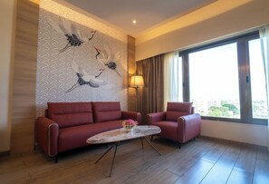 A hotel room with a red sofa, a matching armchair, a marble coffee table, and a large window with curtains. - Pride Elite Chhatrapati Sambhajinagar (Chhatrapati Sambhajinagar)
