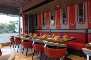Ein Restaurant mit einem langen Esstisch, roten Stühlen und einer roten und weißen Farbgestaltung.