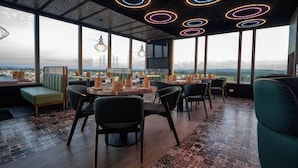 Un espace de restauration moderne avec des tables rondes, des chaises et une vue sur le paysage urbain grâce à de grandes fenêtres.
