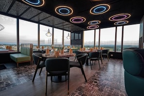 Un espace de restauration moderne avec des tables rondes, des chaises et une vue sur le paysage urbain grâce à de grandes fenêtres.