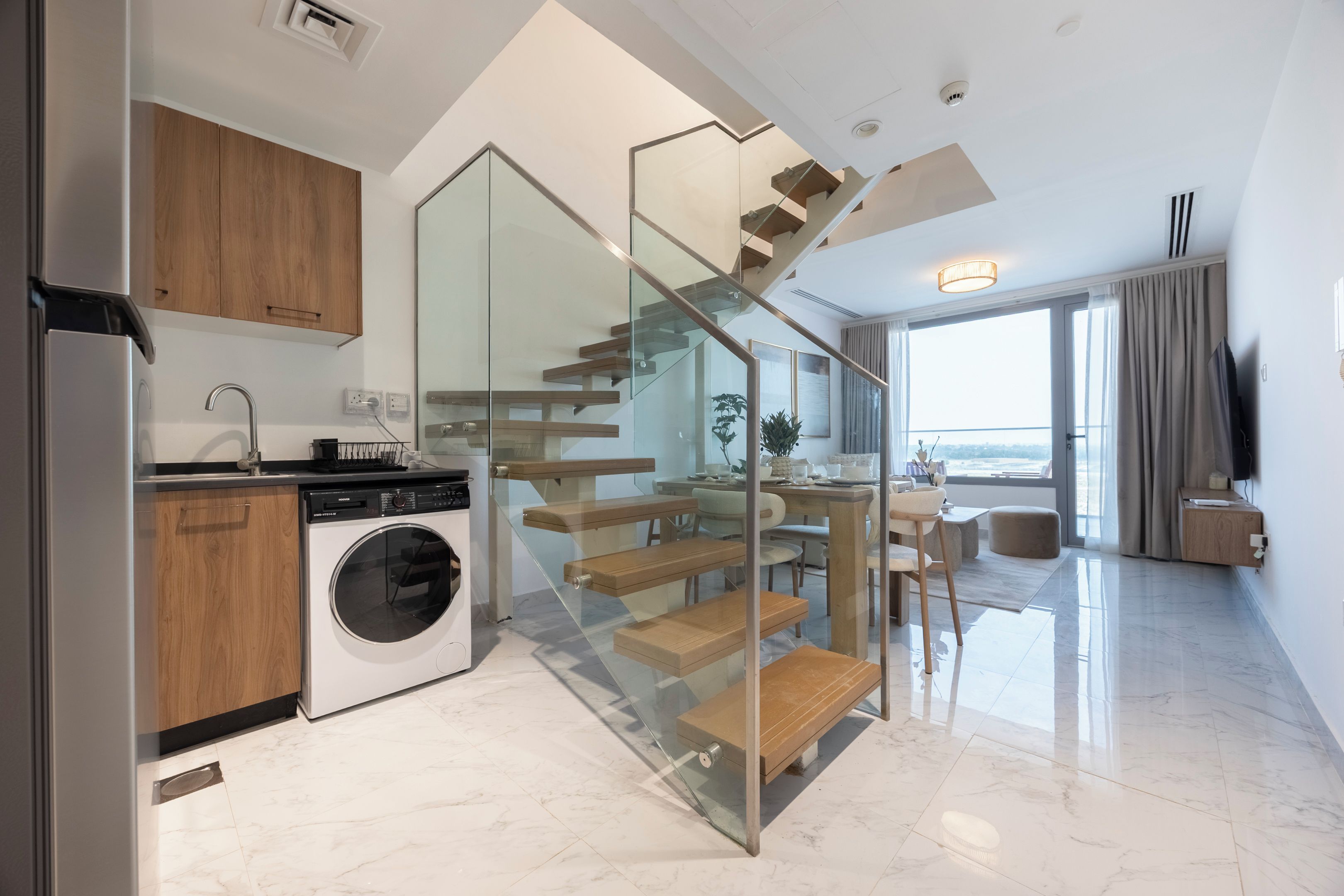 Una cocina moderna con lavadora integrada, una escalera de cristal y un comedor con vistas.