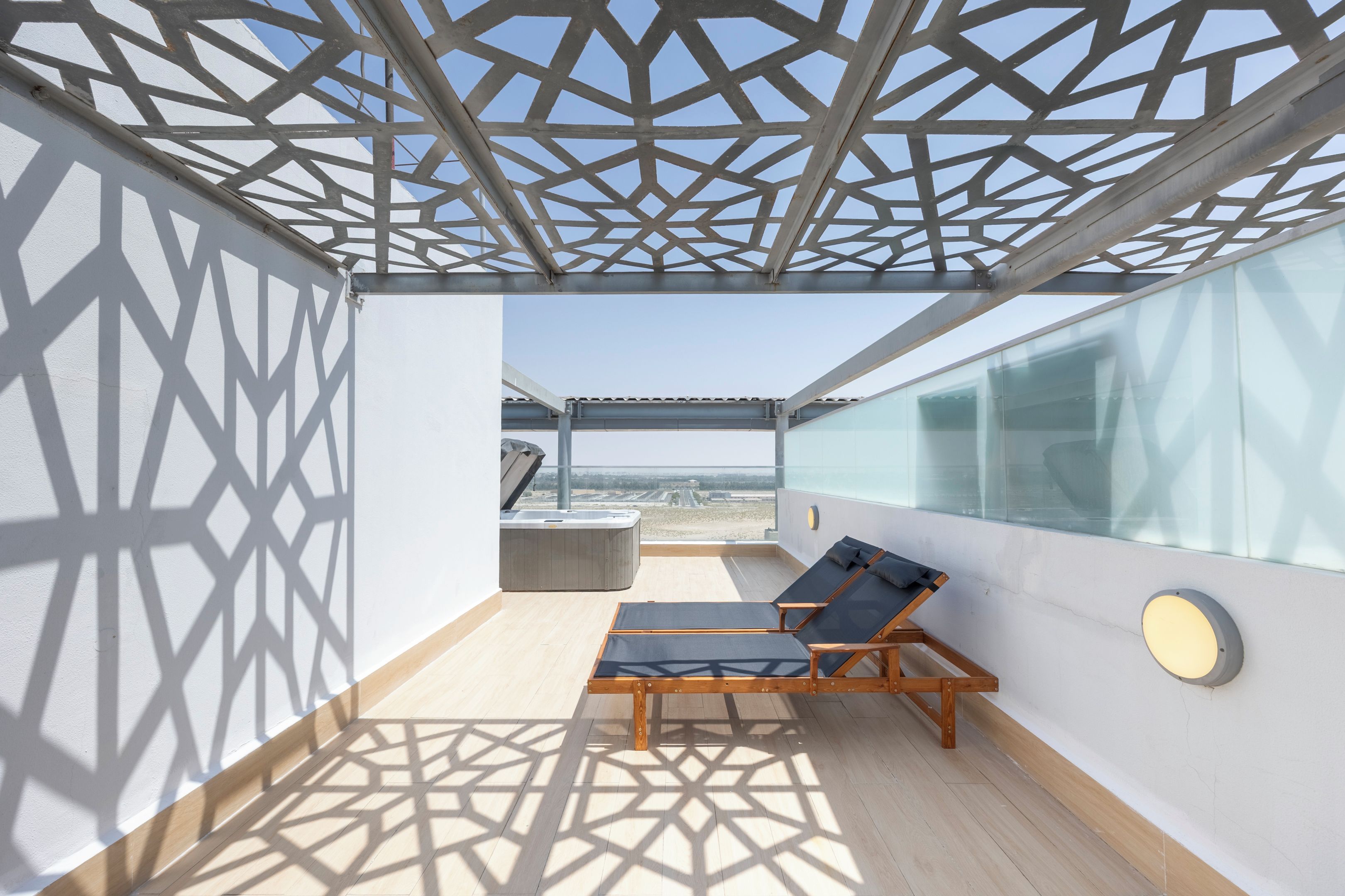 Un balcon ensoleillé avec un plafond aux motifs géométriques, un jacuzzi et un fauteuil de relaxation.