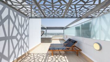 Un balcon ensoleillé avec un plafond aux motifs géométriques, un jacuzzi et un fauteuil de relaxation.