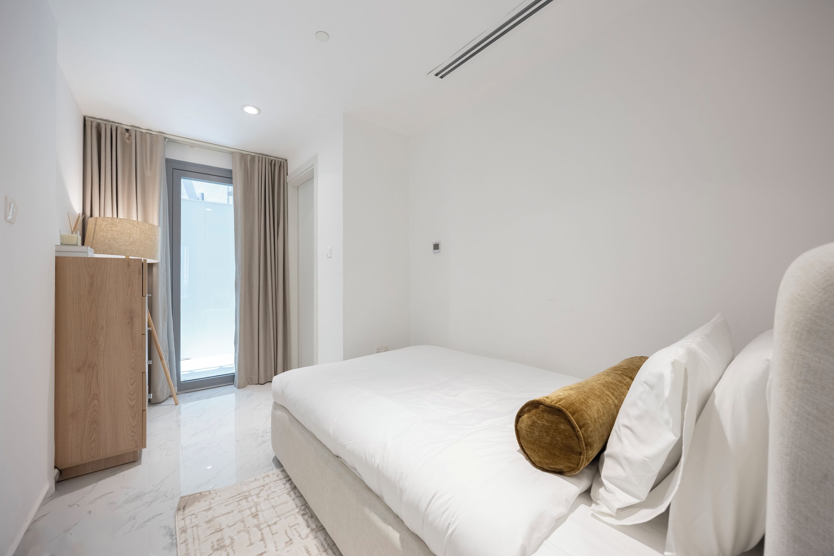 A modern bedroom with a bed, a wooden wardrobe, and a view through a door.