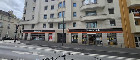 A multi-story building with a 'franprix' store on the ground floor, a bike parking area in front, and a traffic light.