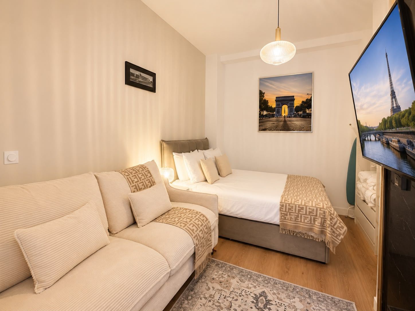 Ein Hotelzimmer mit einer Couch, einem Bett, einem Fernseher und einem Bild des Eiffelturms.