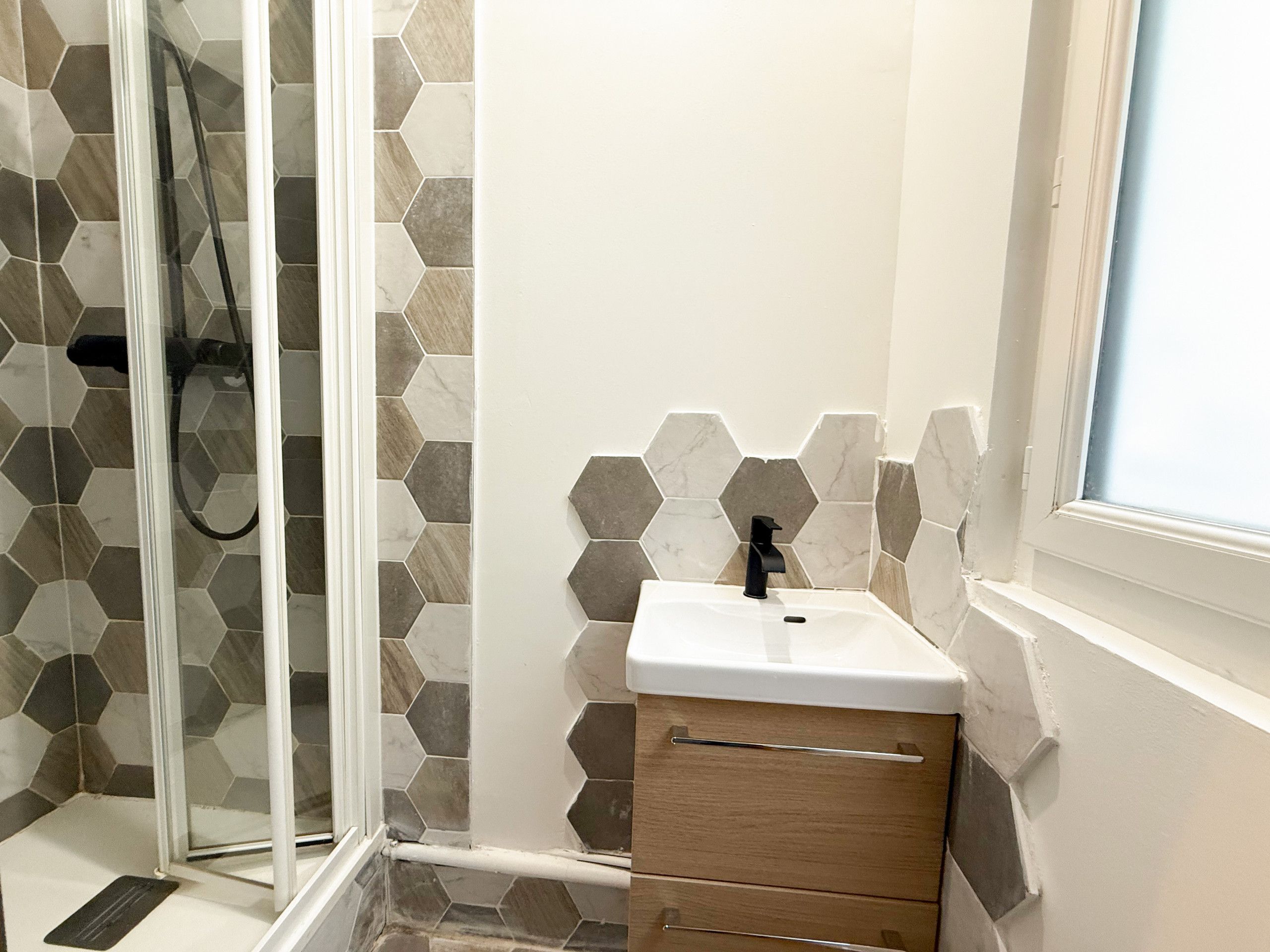 Une salle de bain avec une douche à parois de verre, un lavabo blanc avec un robinet noir et un meuble en bois.