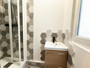 Une salle de bain avec une douche à parois de verre, un lavabo blanc avec un robinet noir et un meuble en bois.