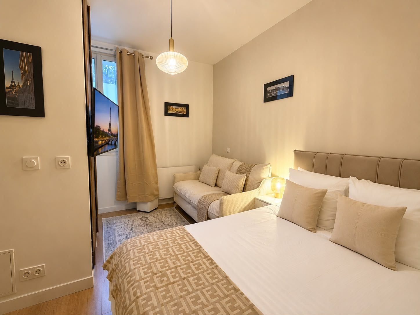 A bedroom with a bed, a sofa, a hanging light fixture, and a window with curtains.