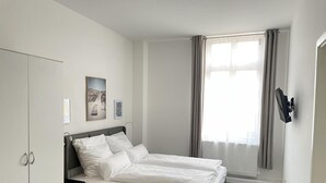 Ein modernes Schlafzimmer mit Bett, Kleiderschrank, Schreibtisch und einem fenster mit Vorhängen.