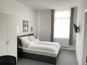 A modern bedroom with a bed, a wardrobe, a desk, and a window with curtains. - Hotel am Bahnhof Stuttgart-ditzingen (Ditzingen)
