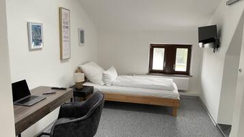 A small, modern room with a bed, a desk with a laptop, a chair, and a TV mounted on the wall.