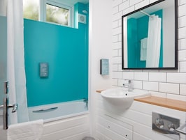 Un baño con una bañera blanca, un lavamanos con encimera de madera, un espejo y una ventana con vistas a la vegetación.