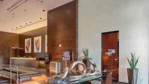 Um lobby de hotel moderno com balcão de recepção, área de estar e uma mesa de centro de vidro com arte de metal abstrata.