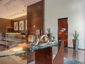 A modern hotel lobby with a reception desk, seating area, and a glass coffee table with abstract metal art. - The Adele Palazzo Suite at Palms Place (Las Vegas)