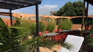 An outdoor seating area with a lounge chair, red chairs, and tables, surrounded by greenery and a brick wall. - Hotel and Spa Le Gambetta (Paris)