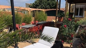 A sunlit outdoor seating area with a lounge chair, red chairs, and a table.