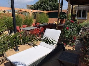 Un espace extérieur ensoleillé avec des sièges, comprenant un fauteuil de relaxation, des chaises rouges et une table.