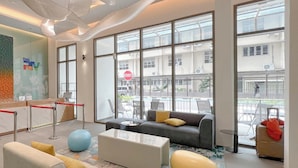 En moderne hotellobby med receptionsdisk, siddeområde og store vinduer med udsigt til gaden.